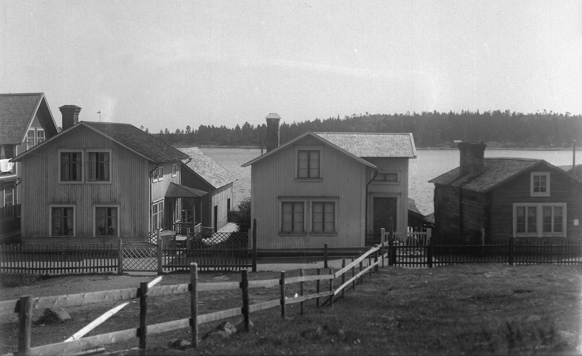 Bilden visar gaveln på tre hus längs en väg. I förgrunden syns staket och grindar.