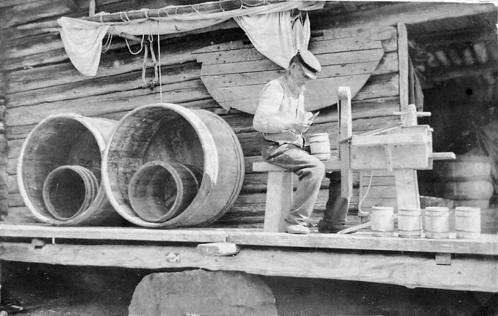 Bilden visar en man som sitter ner och tillverkar en träkagge