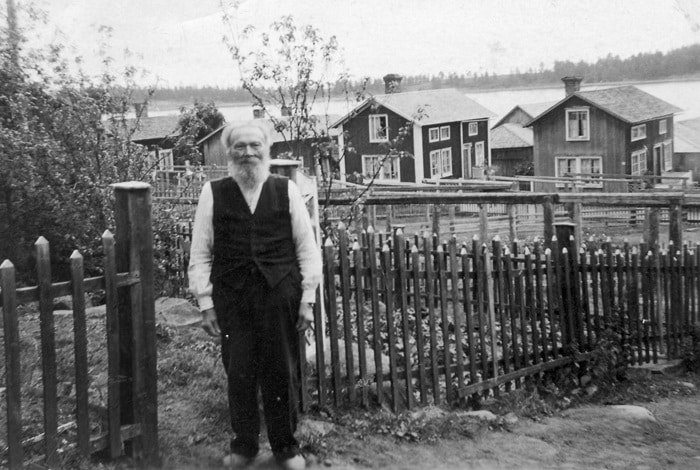Bilden visar en äldre man som står framför ett trästaket