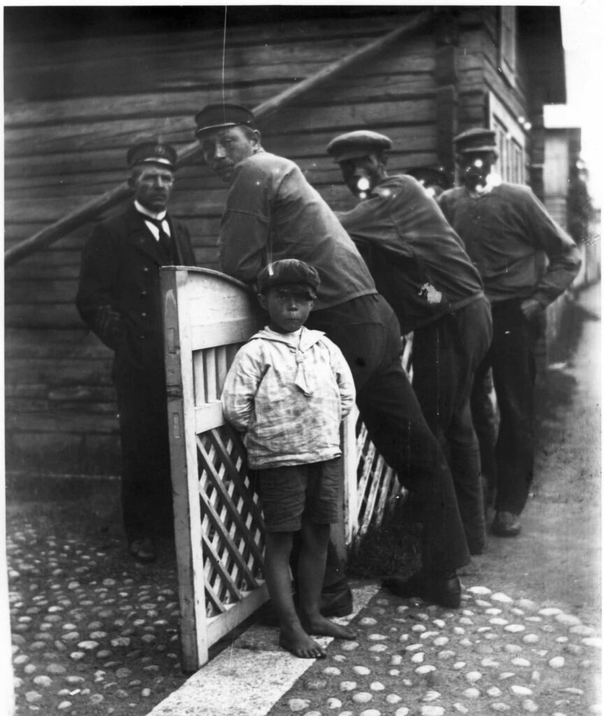 På bildens syns fyra män och ett barn utanför ett hus. En av männen är lots och de övriga fiskare.