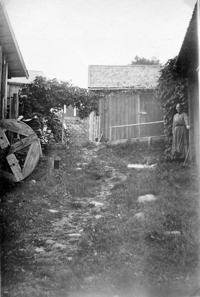 Bilden visar en äldre kvinna utanför ett hus.