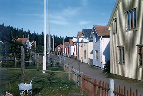 Bilden visar trähus längs en grusväg. I förgrunden en dockvagn