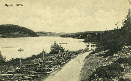 Bilden som är ett vykort visar en sjö, grusväg och skog