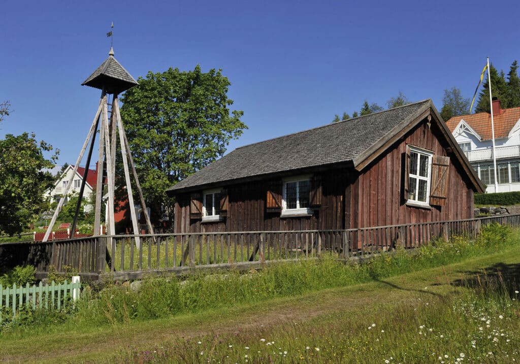 Ett gammalt kapell med träfasad. Vid kapellet en klockstapel