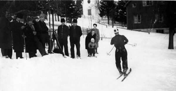 Bilden visar snö, en skidåkare och några som ser på.