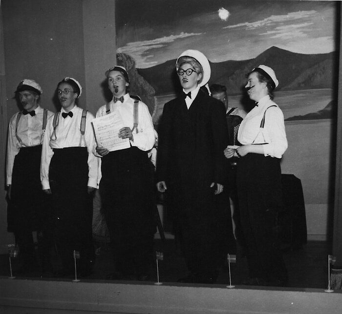 Bilden visar fem utklädda personer som står på en scen och sjunger