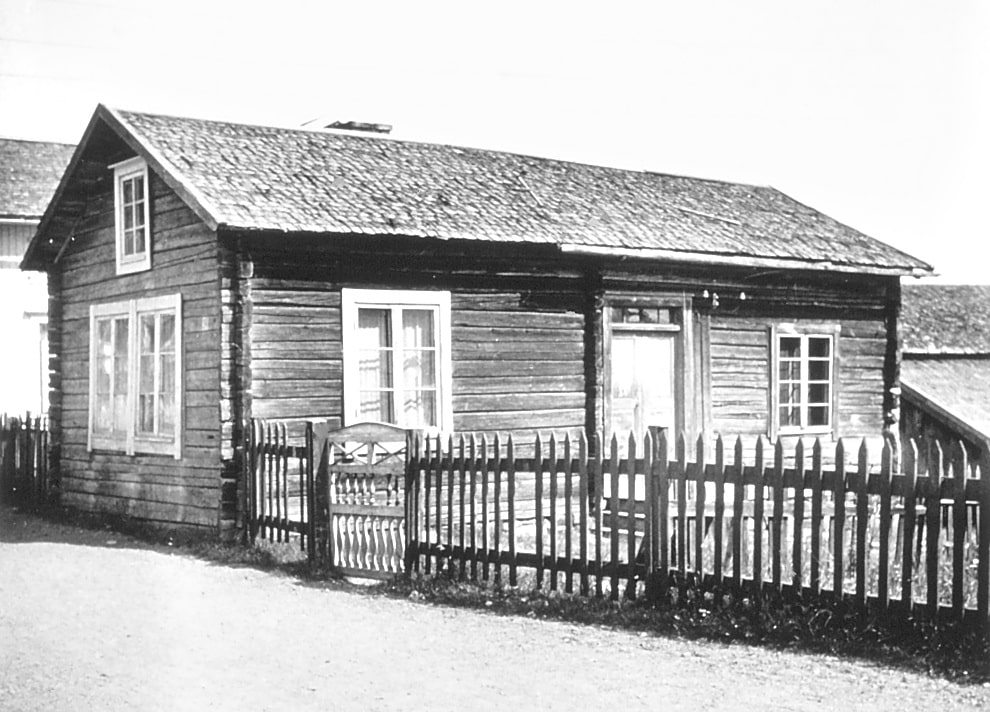 Bilder visar ett litet timrat hus som står längs en grusväg, staket och grind.