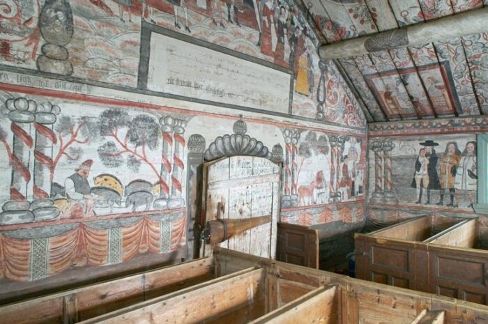 Bilden visar en interiör från Ulvö kapell. Väggarna har gamla målningar i många färger.